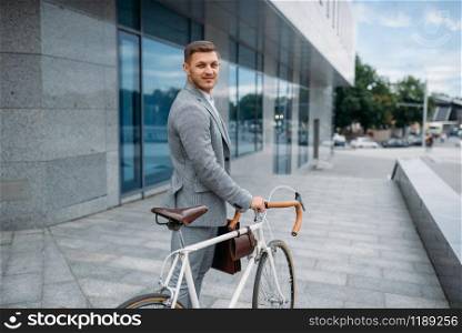 One businessman in suit with briefcase cycling in downtown. Business person riding on eco transport on city street. One businessman with briefcase cycling in downtown