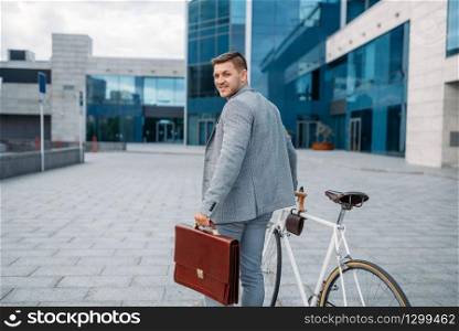 One businessman in suit with briefcase cycling in downtown. Business person riding on eco transport on city street. One businessman with briefcase cycling in downtown