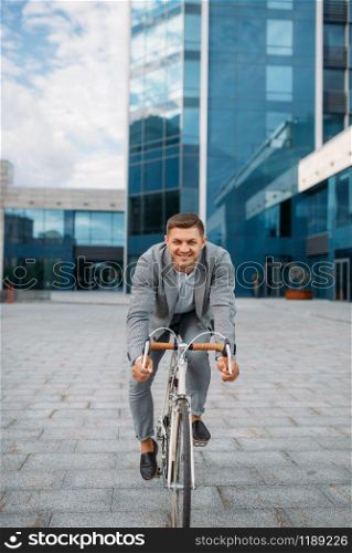 One businessman poses on bicycle in downtown. Business person riding on eco transport on city street
