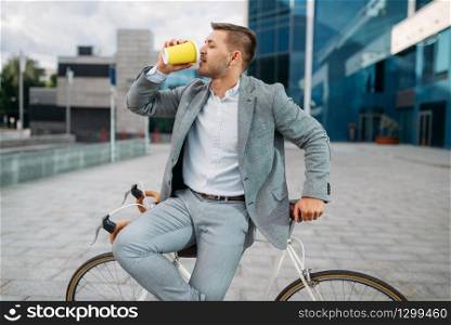 One businessman with bike drinks coffee in downtown. Business person riding on eco transport on city street