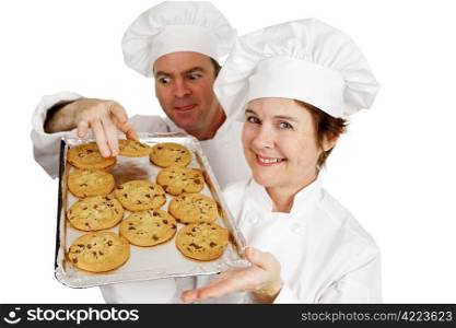 One chef sneakes up and steals a chocolate chip cookie from another. Isolated on white.