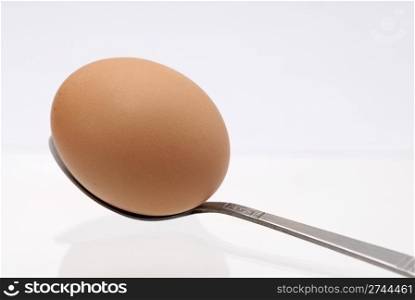 One egg balancing on a teaspoon against white background.