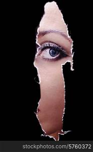 One eye of a young woman spying through a hole in the wall