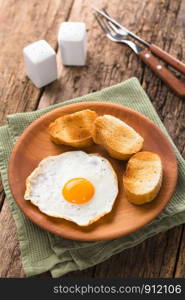 One fresh fried egg sunny side up with toasted baguette slices on the side served on wooden plate, cutlery, salt and pepper shaker in the back (Selective Focus, Focus on the front of the egg yolk). Fried Egg with Toasted Bread