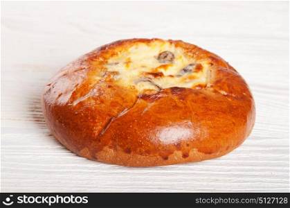 One fresh homemade bun with cottage cheese and raisins on a wooden table