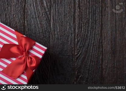 One gift box with an red big ribbon on old wooden dark brown background for christmas, close up view holidays concept, orizontal version