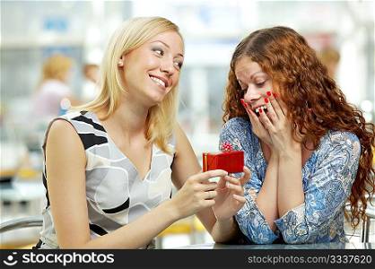 One girlfriend presents a gift another in cafe