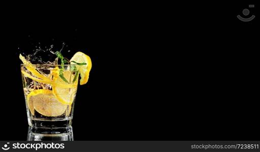 One glass with lemonade or mojito, a cocktail with lemon and mint. Cold drink on a black background. Spray from falling ice in a drink. Copy space, close up.