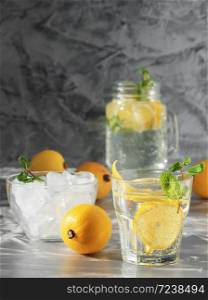 One glass with lemonade or mojito cocktail with lemon and mint and cup with ice. Cold refreshing drink or beverage with ice on dark background. Copy space