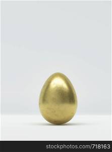 One golden Easter egg on grey background in close-up, balanced vertically on its blunt end
