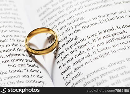 One golden wedding ring on Holy bible book with heart shaped shadow close up. Golden wedding ring on bible book
