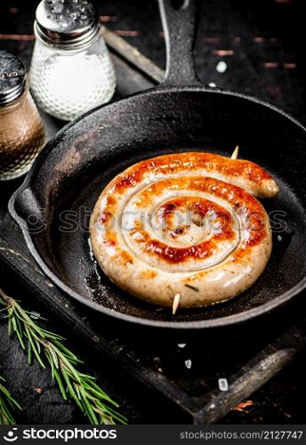 One grilled sausage in a frying pan with rosemary and spices. On a black background. High quality photo. One grilled sausage in a frying pan with rosemary and spices.