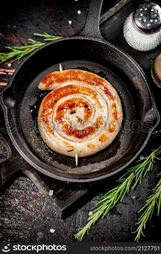 One grilled sausage in a frying pan with rosemary and spices. On a black background. High quality photo. One grilled sausage in a frying pan with rosemary and spices.