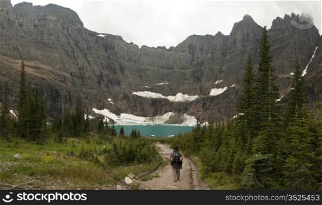 One hiker walking towards Iceberg Lake in Glacier National Park. The headwall of the valley is a perfect bowl formed by cliffs with hanging glaciers; the ice calves off to form icebergs in the lake.