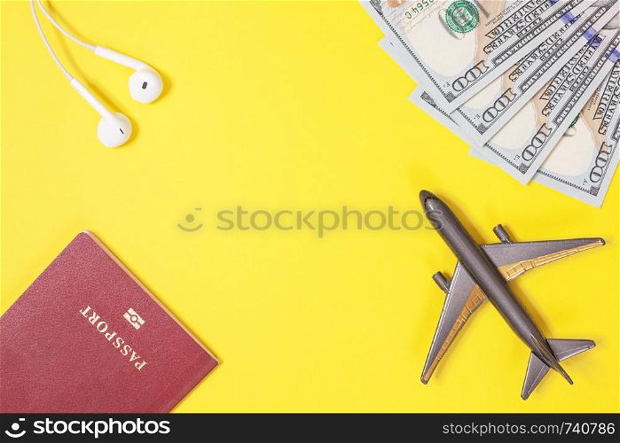 One hundred dollar bills, airplane, headphones, foreign passport on bright yellow paper background. Copy space. Travel and budget trip concept, flat lay. Hand luggage, minimalism, frame of objects