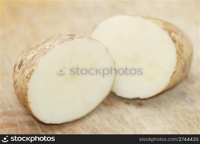 One Kestrel potato cut in half on chopping board. Focus on first half.