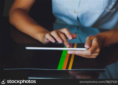 One light-skinned hand belonging to a woman holds a large tablet while the other hand uses a pointer finger to access something on the tablets touch screen display. The tablet has a gray case and a glass screen. The woman in blue shirt.. Woman working on digital tablet