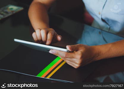 One light-skinned hand belonging to a woman holds a large tablet while the other hand uses a pointer finger to access something on the tablets touch screen display. The tablet has a gray case and a glass screen. The woman in blue shirt.. Woman working on digital tablet