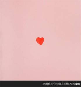 one little heart cut out of red paper on background from light pink pastel paper