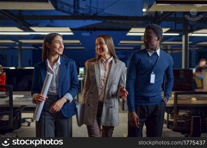 One man and two women in night office. Smiling male and female workers, dark business center interior on background, modern workplace. One man and two women in night office