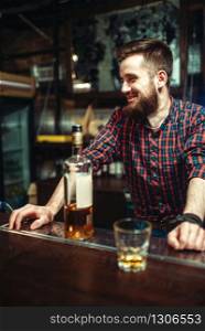 One man with bottle of alcohol beverage in hand standing at the bar counter. Male person in pub, alcoholism, drunkenness. One man standing at the bar counter, drunkenness