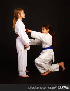 one more experienced karate girl helps another tie a kimono belt correctly. karate girl help