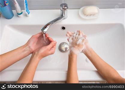 One pair of hands washes away foam, another pair of hands soaps