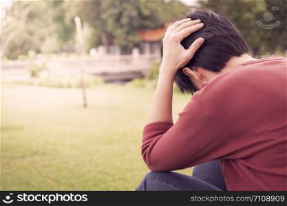 One person wears a red shirt, grabs his head with stress In the garden at sunset. Mental health, depression concept.