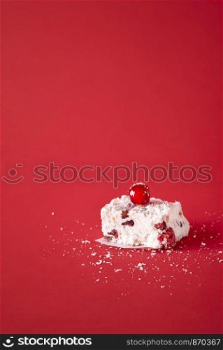 One piece of Australian Xmas dessert, homemade with coconut and dried fruits, on a red background. Close-up with traditional white Christmas cake.