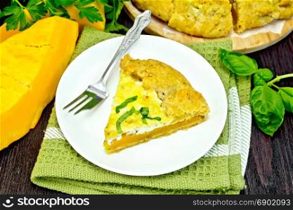 One piece of the pie of pumpkin, salty feta cheese, eggs, cream and herbs in a plate on a napkin, basil on a dark wooden board