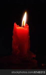 One red candle burning in the darkness closeup