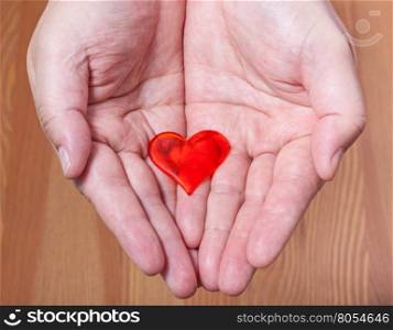 one red heart on male palms with wooden background