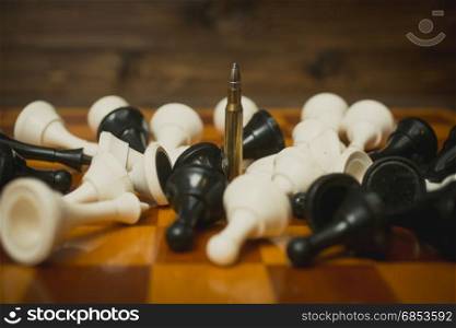 One riffle bullet on chessboard among lying chess pieces