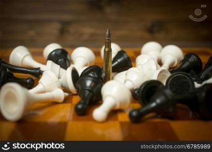 One riffle bullet on chessboard among lying chess pieces. Concept of military power