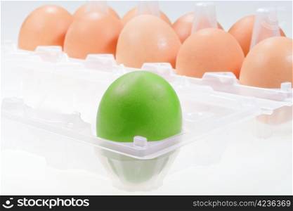 one separate green chicken egg against several brown eggs