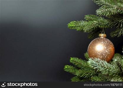 One single Christmas bauble hanging on fresh green branch of Christmas tree near dark black background with copy space, Merry Christmas, Holiday concept space for text. One single Christmas bauble hanging on fresh green branch of Christmas tree near dark black background with copy space, Merry Christmas, Holiday concept
