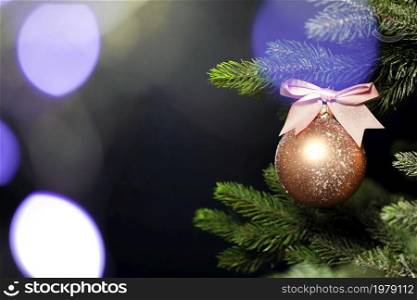 One single Christmas bauble hanging on fresh green branch of Christmas tree near dark black background with copy space, Merry Christmas, Holiday concept space for text. One single Christmas bauble hanging on fresh green branch of Christmas tree near dark black background with copy space, Merry Christmas, Holiday concept
