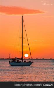 One single sailing boat on sea at setting orange sun