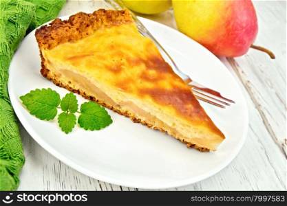 One slice of pear cake with cream sauce in white plate, fork, pear and mint, napkin on the background light wooden boards