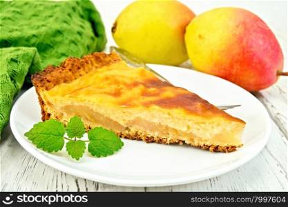 One slice of pear cake with cream sauce in white plate, fork, pear and mint, napkin on a wooden boards background