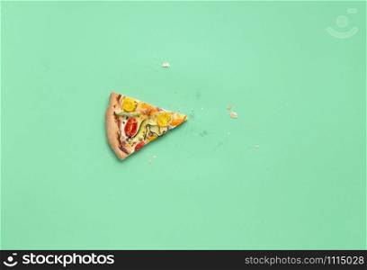 One slice of pizza primavera and crumbs on green background. Above view of vegetarian spring pizza leftovers. Single slice of pizza. Italian cuisine