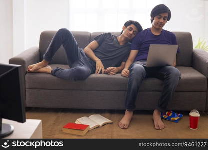 One teenage boy using the laptop while the other leaning at home