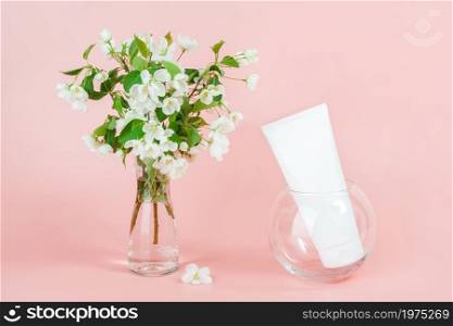 One white blank cosmetic tube bottle and blooming branch in vase on pink background. Natural Organic Spa Cosmetic Beauty Concept. Mockup Front view.. One white blank cosmetic tube bottle and blooming branch in vase on pink background. Natural Organic Spa Cosmetic Beauty Concept. Mockup Front view