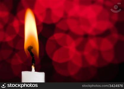 One white burning candle, red glistering background.