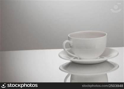 one white cup and saucer on a light background with reflection. cup and saucer on a light background