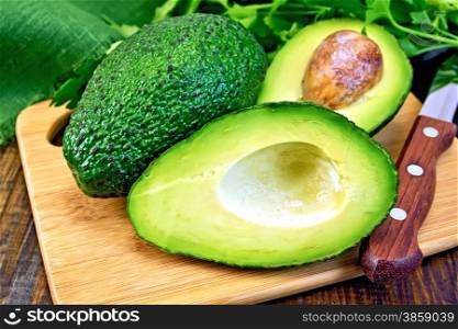 One whole and one cut in half avocado, knife, parsley, napkin on a wooden boards background