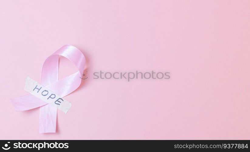 One wide satin pink ribbon with sticky tape with the word  hope lies on the left on a pink background with copy space on the right, flat lay close-up. Concept for world cancer day, breast cancer.. Pink ribbon with sticky tape and the word  hope on a pink background.