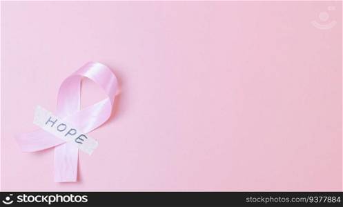One wide satin pink ribbon with sticky tape with the word  hope lies on the left on a pink background with copy space on the right, flat lay close-up. Concept for world cancer day, breast cancer.. Pink ribbon with sticky tape and the word  hope on a pink background.