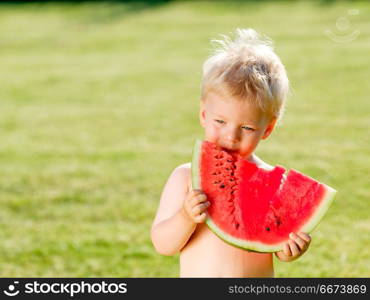 One year old baby boy eating watermelon in the garden. Portrait of toddler child outdoors. Rural scene with one year old baby boy eating watermelon slice in the garden. Dirty messy face of happy kid.