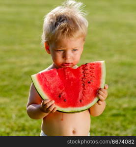 One year old baby boy eating watermelon in the garden. Portrait of toddler child outdoors. Rural scene with one year old baby boy eating watermelon slice in the garden.